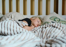 a little girl sleeping in a bed with a blanket